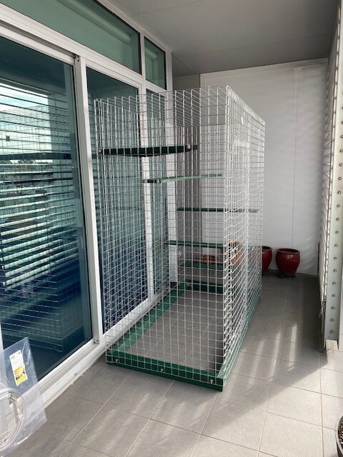 Galvanised Catnip enclosure clipped onto an apartment balcony beside sliding doors